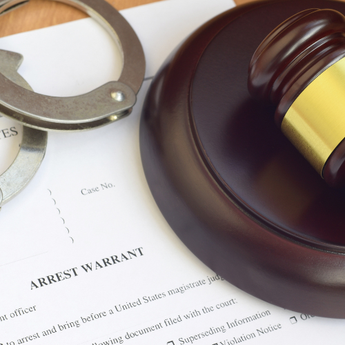 Handcuffs on arrest warrant next to a gavel, symbolizing law and order.