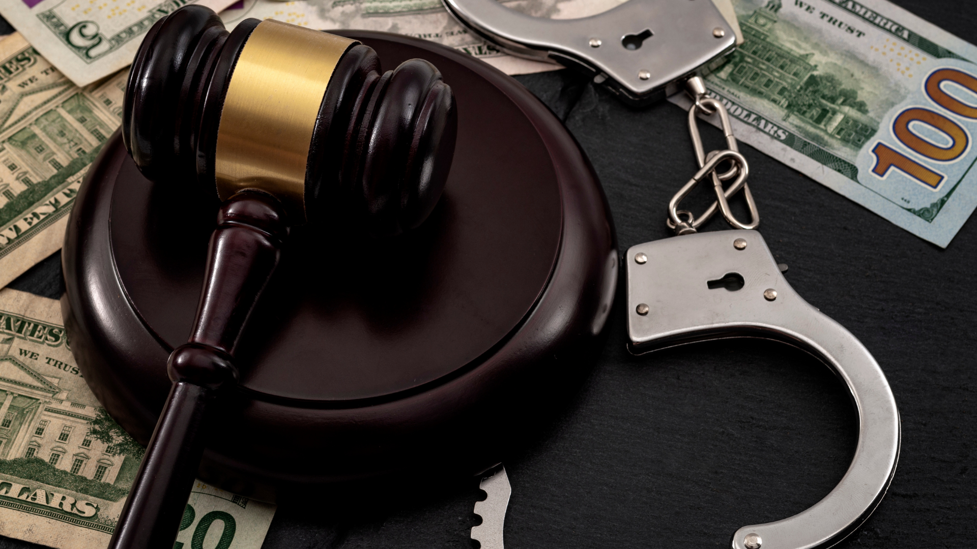 Gavel, handcuffs, and cash on a dark surface, symbolizing crime and legal issues.