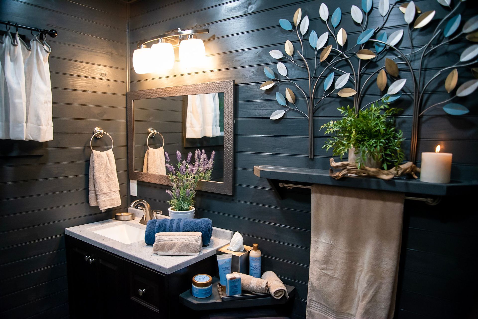A bathroom with a sink , mirror , towels and a candle.