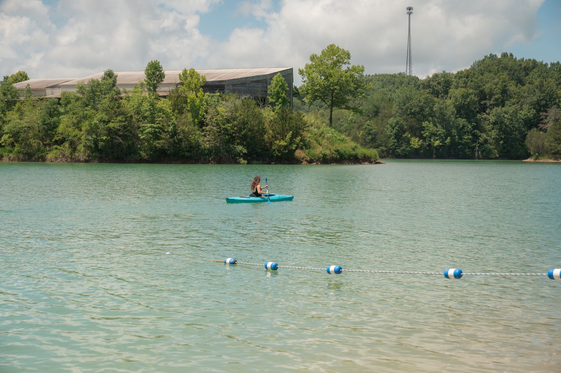 Two people are kayaking on a lake with trees in the background.