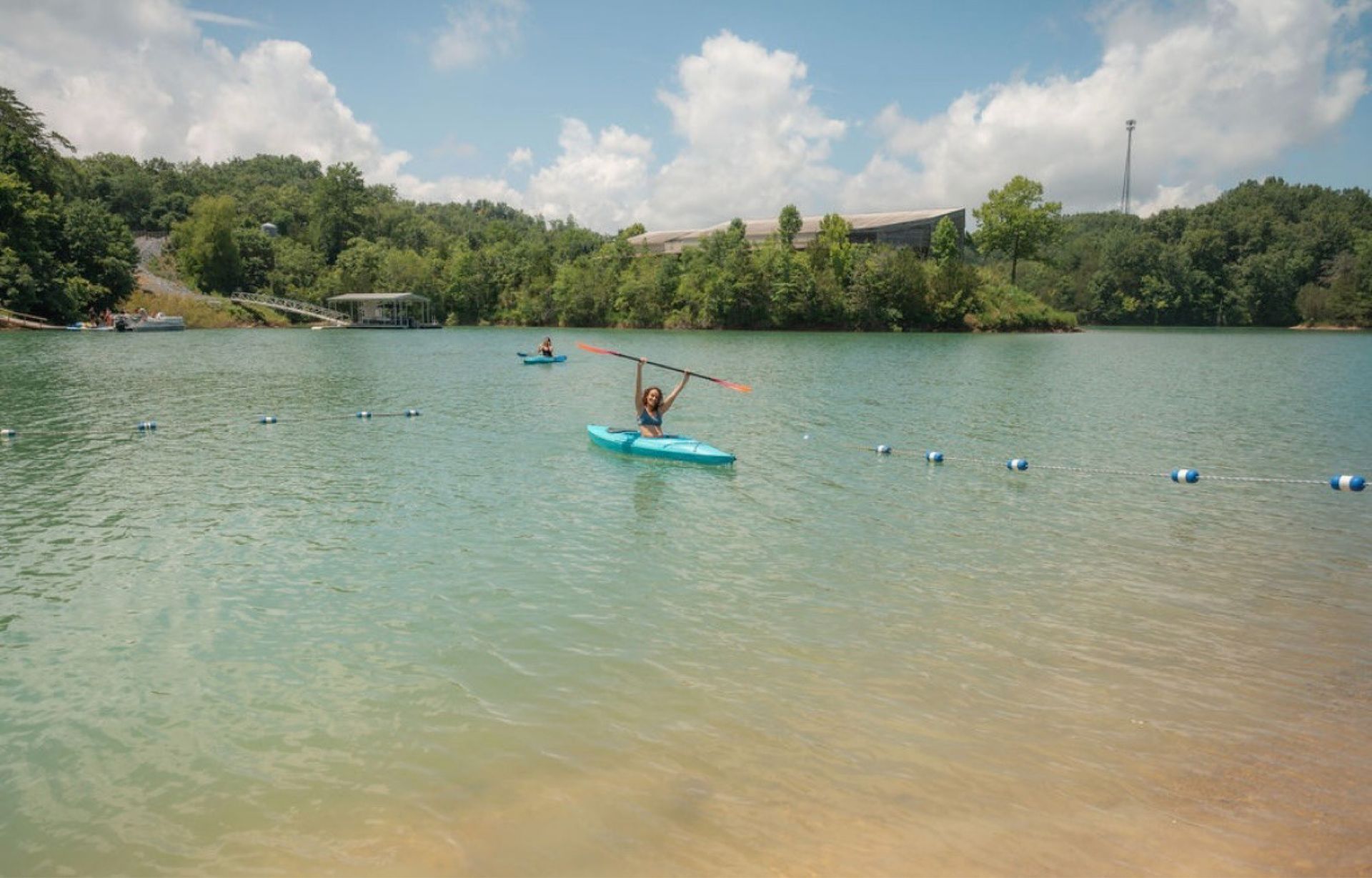 Person on a blue paddleboard in a calm lake surrounded by green trees under a cloudy sky
