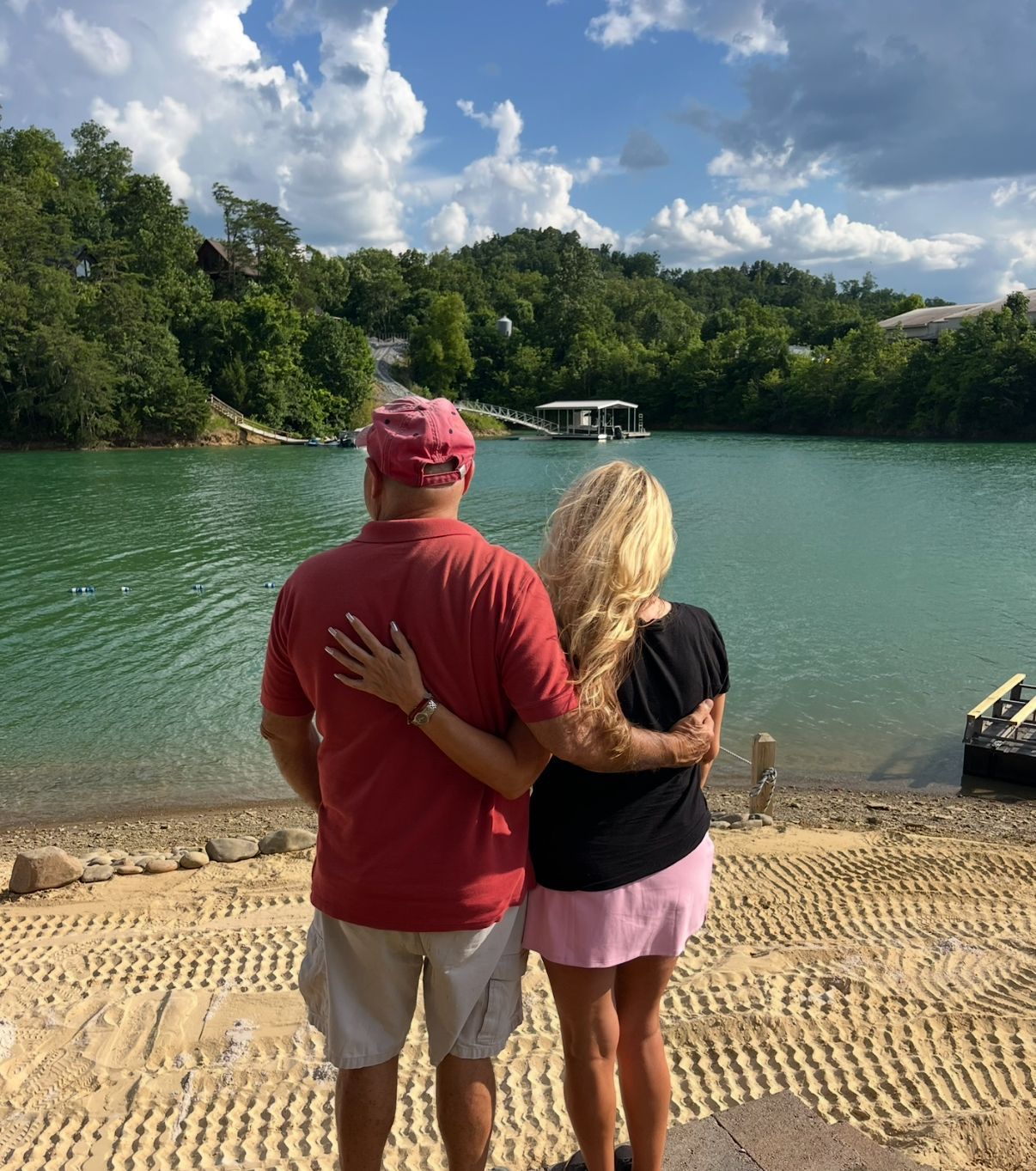 Couple with arms around each other, overlooking a green lake in the mountains.