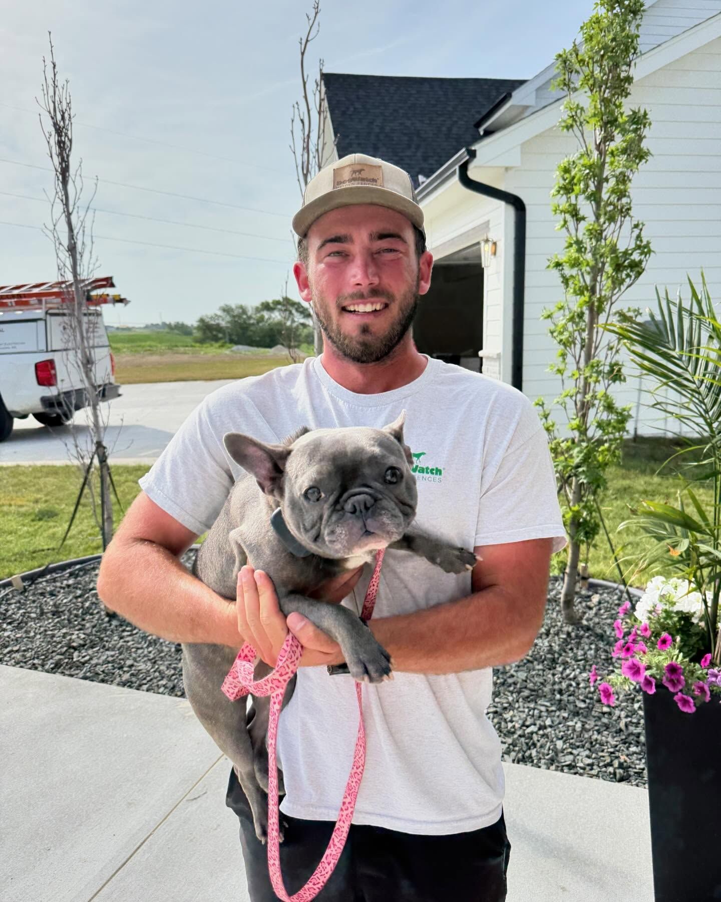Man holding a gray French Bulldog. They are outside, smiling.