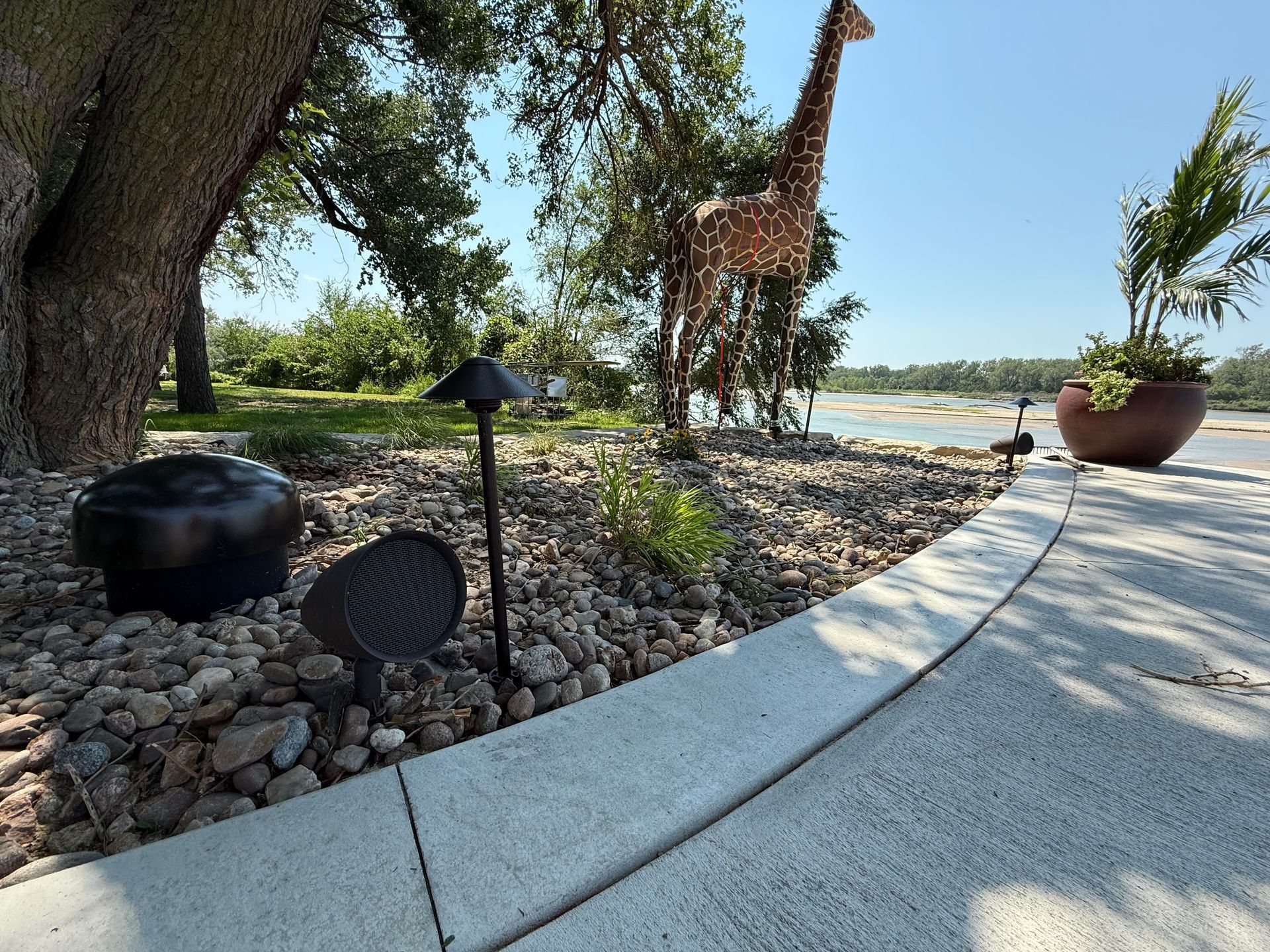 Landscape with a stone-lined bed, concrete path, giraffe statue, and water in the background.