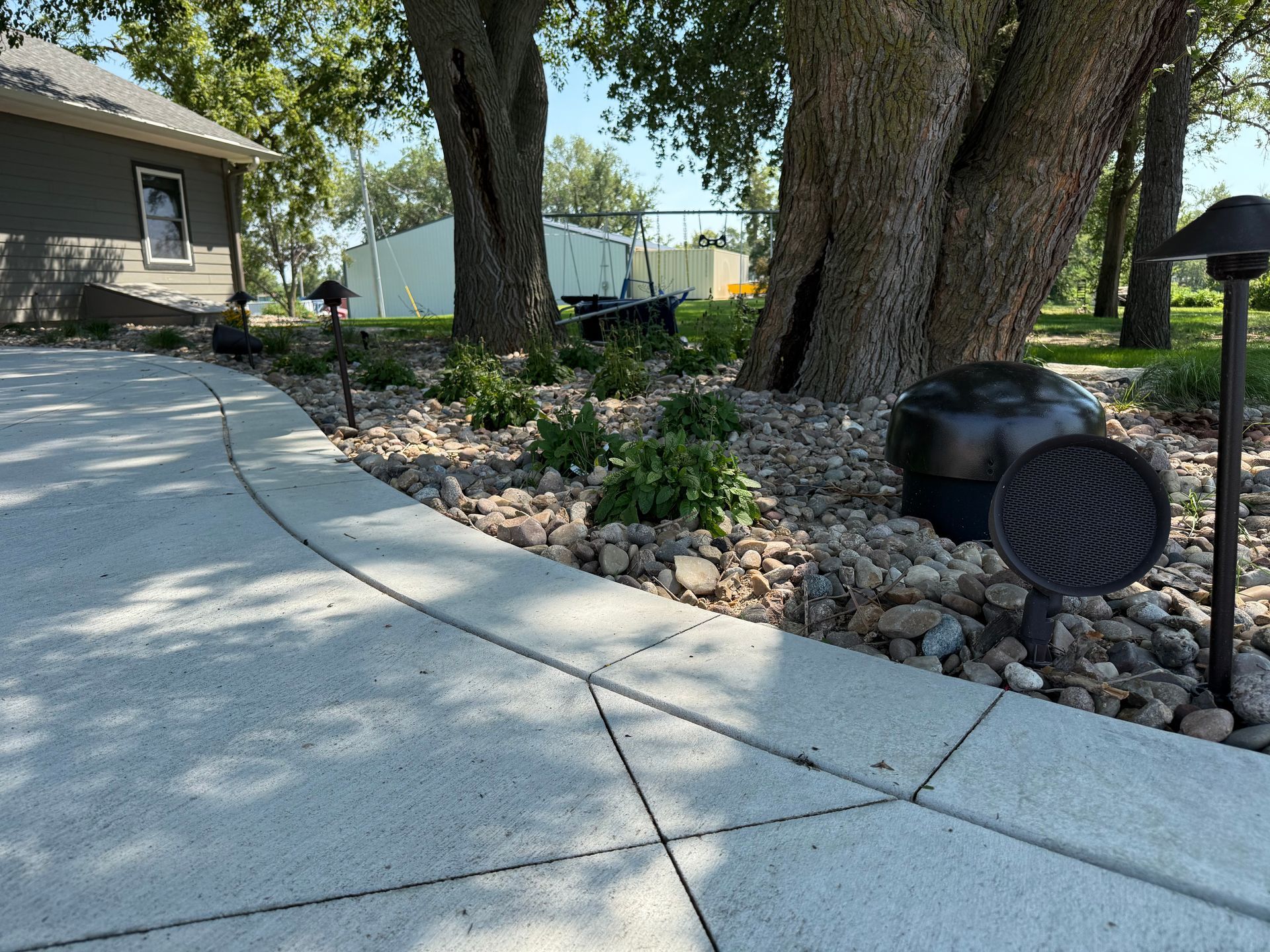A driveway curves past a landscaped area with lighting and mature trees.