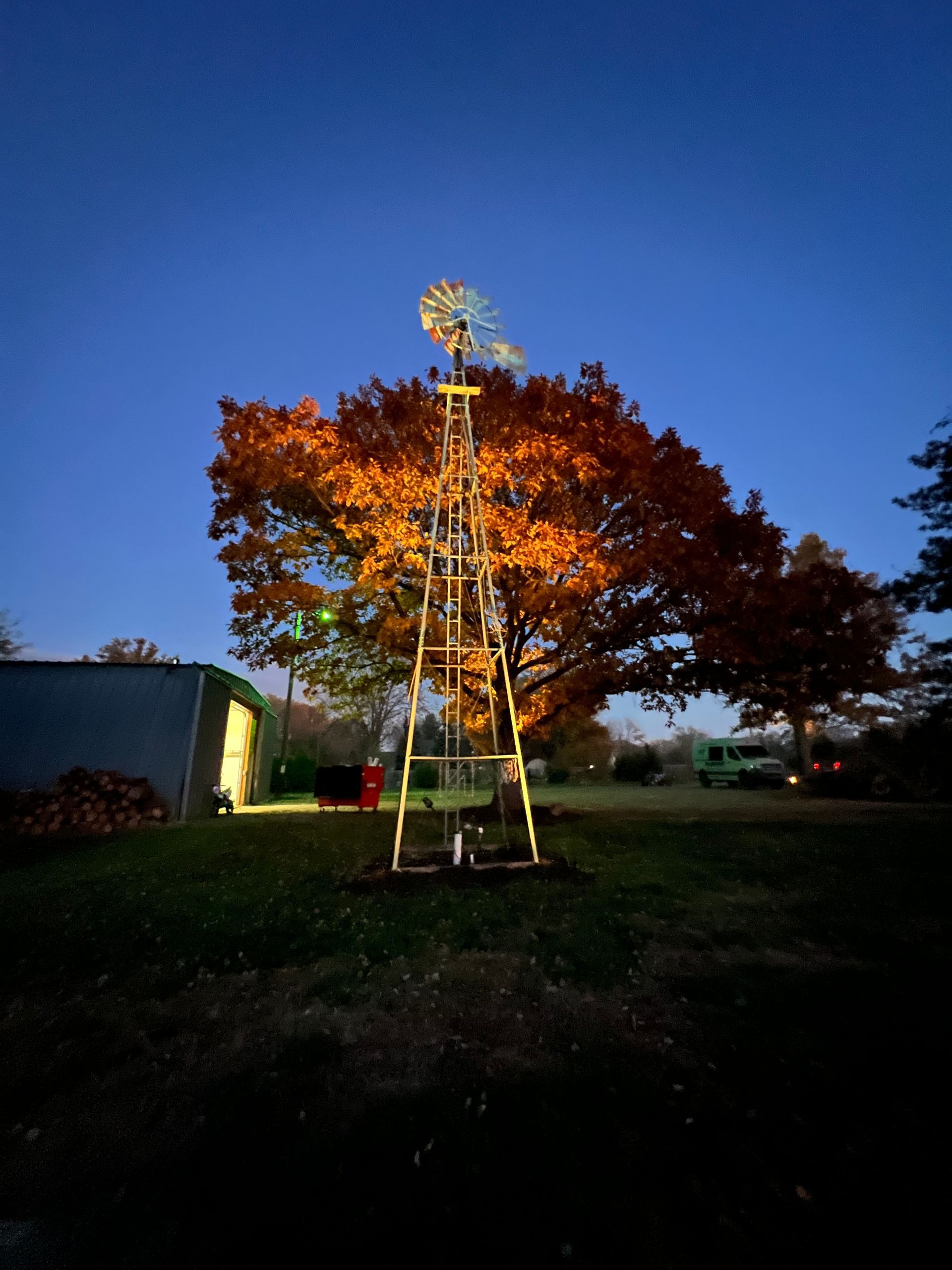 Windmill in front of an autumn tree against a twilight blue sky.