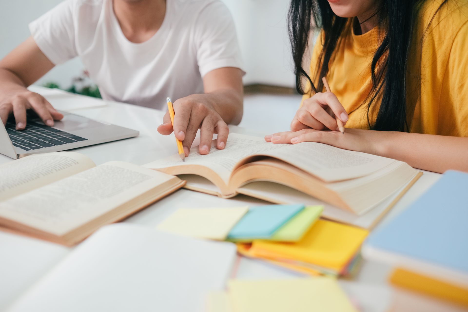 A boy and a girl are sitting at a table with books and a laptop.
