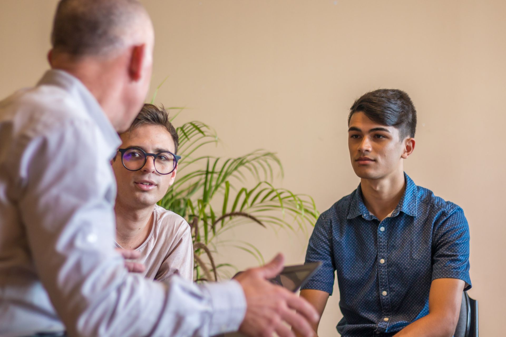 A man is talking to two young men in a room.