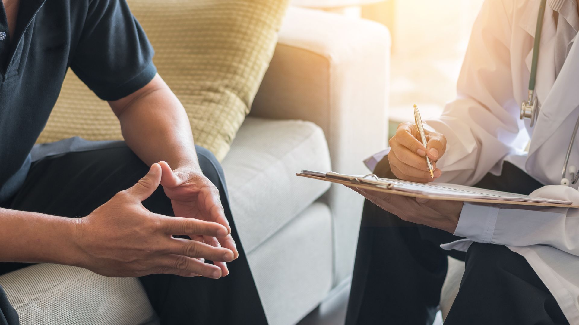A doctor is talking to a patient who is sitting on a couch.