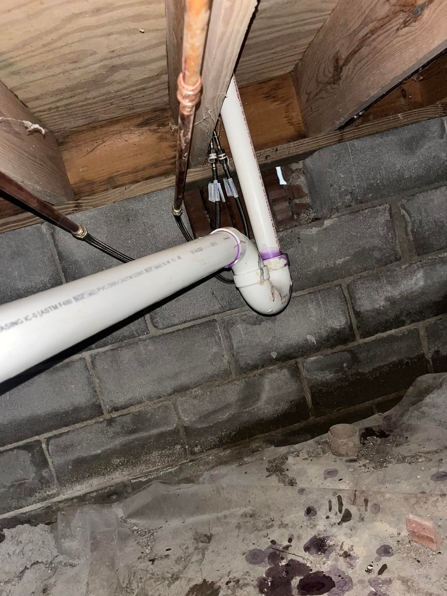White PVC pipes connected to a black wire in a crawl space with cinder block walls.