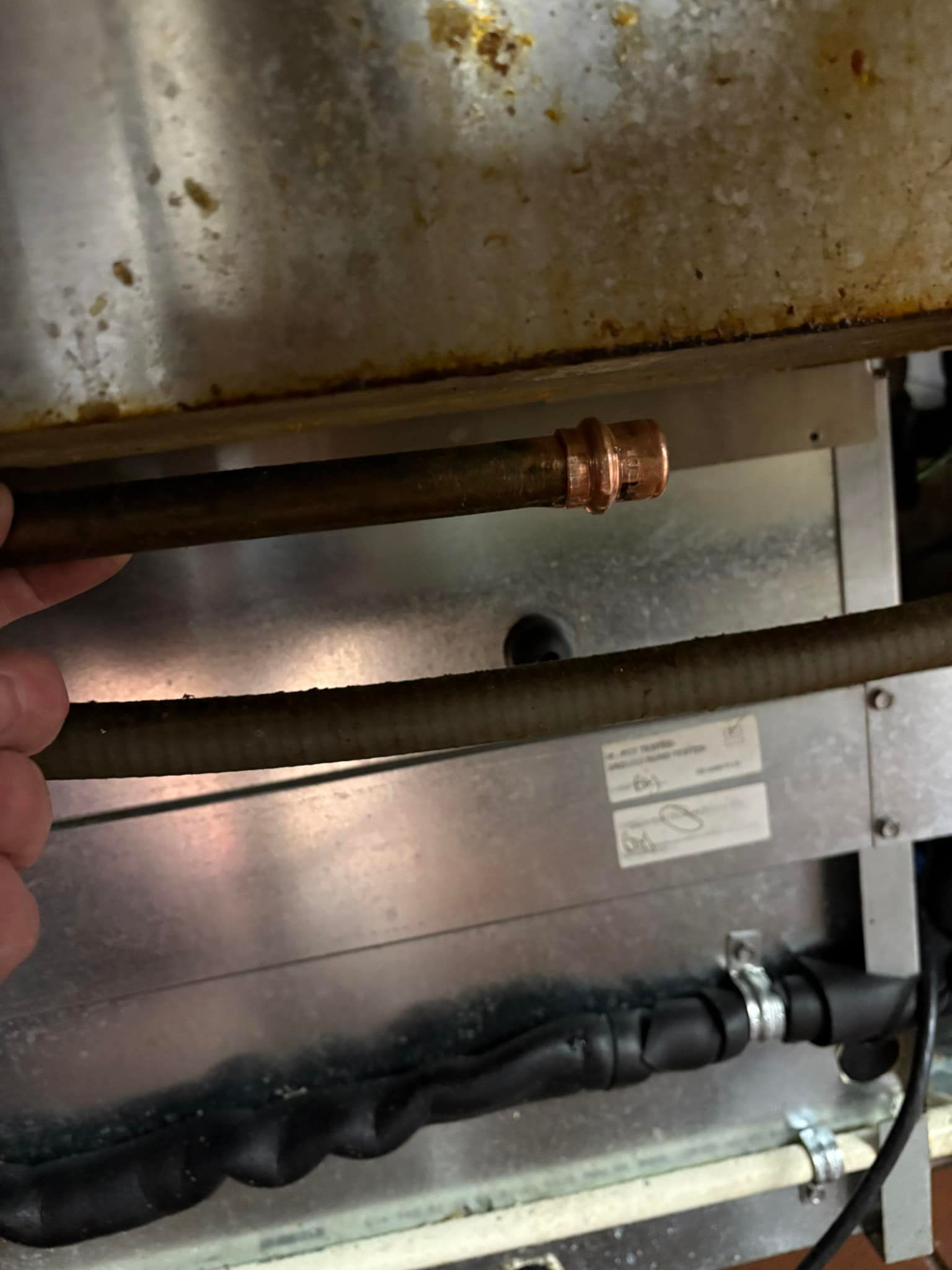 A copper pipe with a fitting, likely for plumbing, is held by a hand inside of a metal appliance.