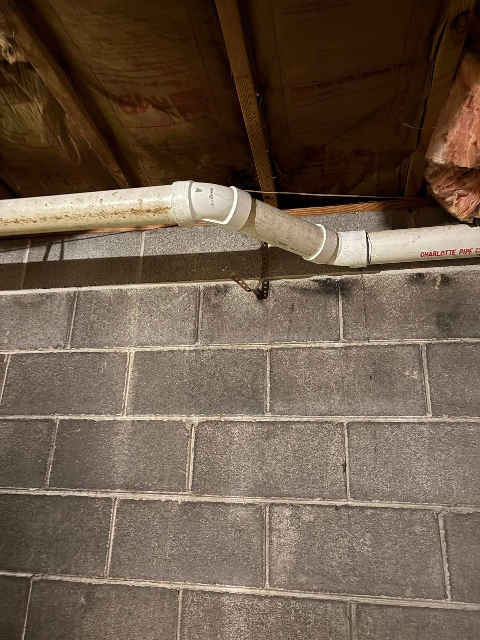 White pipes run across a gray cinder block wall in a basement. The pipes are connected with gray couplings.