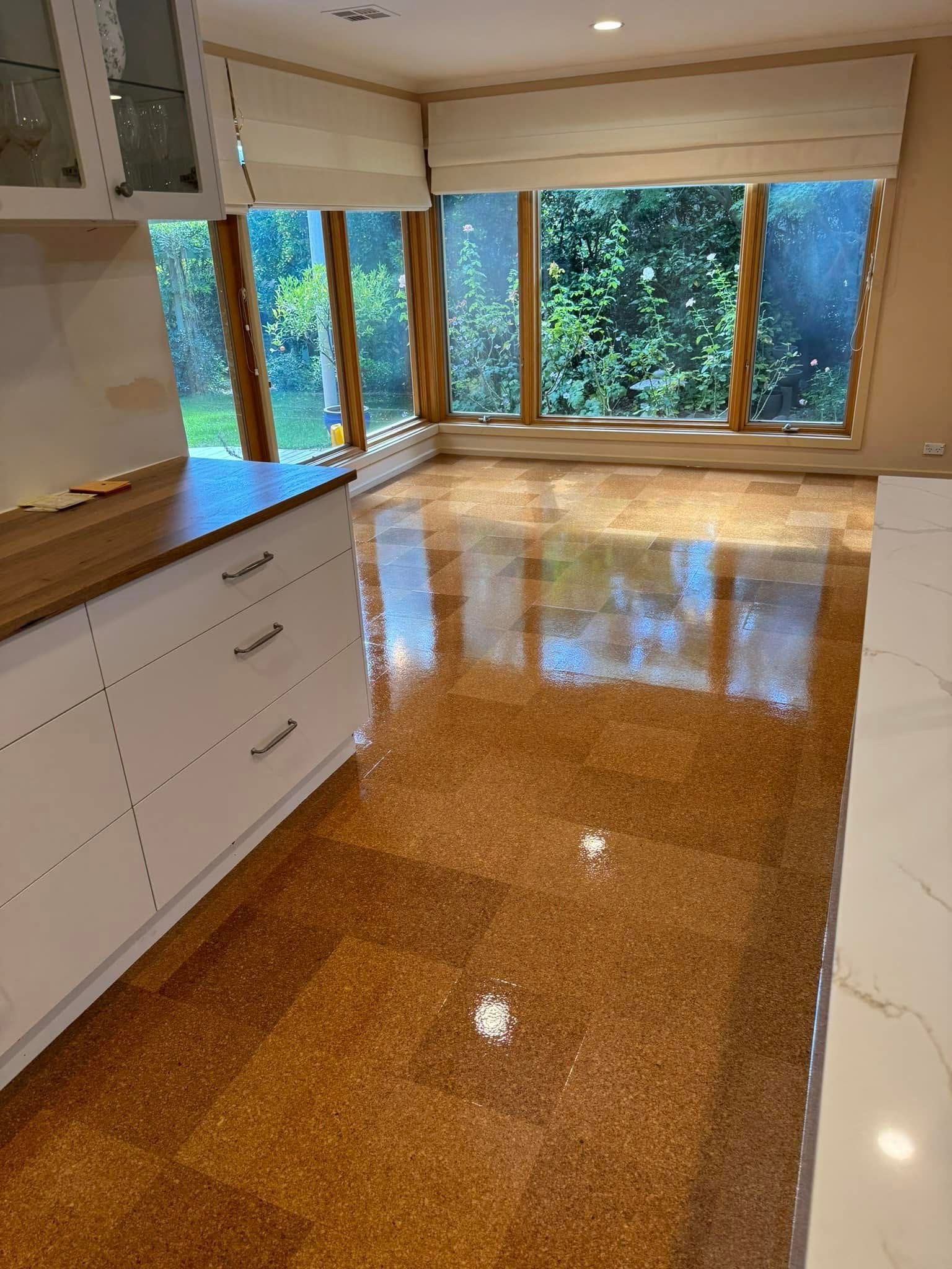 Cork Flooring in A Kitchen with White Cabinets, Light from Large Windows, and A View of Greenery — Canberra Floor Coverings in Queanbeyan West, NSW