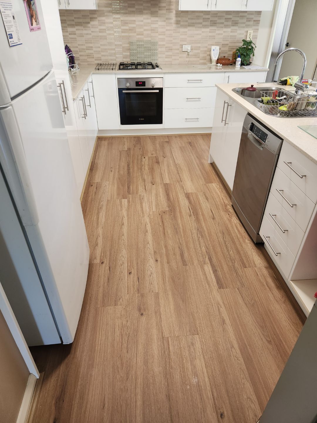 Kitchen with White Cabinets, Wood-Look Floors, Stainless Steel Appliances, and Countertop Workspace — Canberra Floor Coverings in Queanbeyan West, NSW