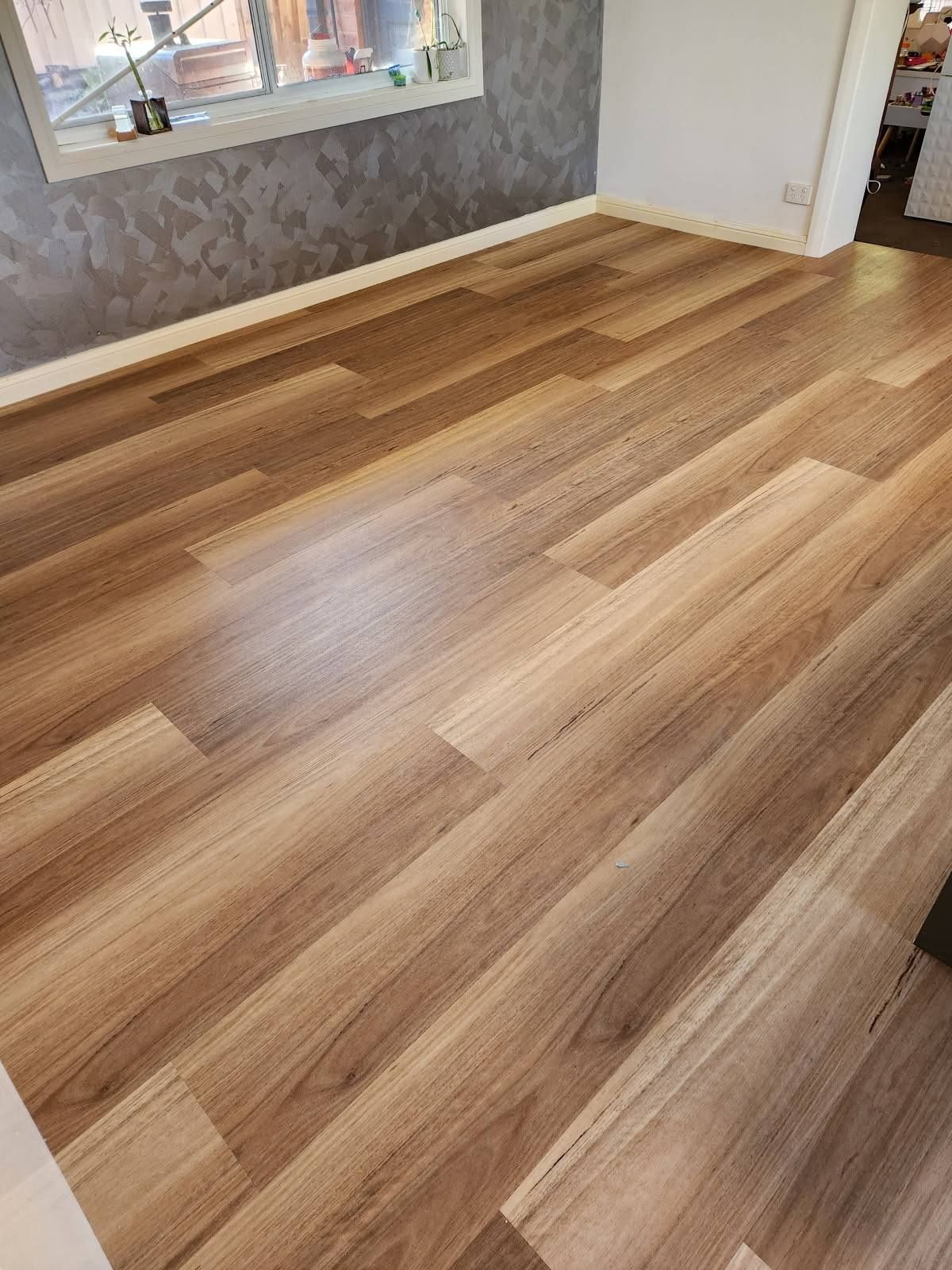 Wooden Laminate Flooring in A Room with A Window and Textured Grey Wallpaper — Canberra Floor Coverings in Queanbeyan West, NSW