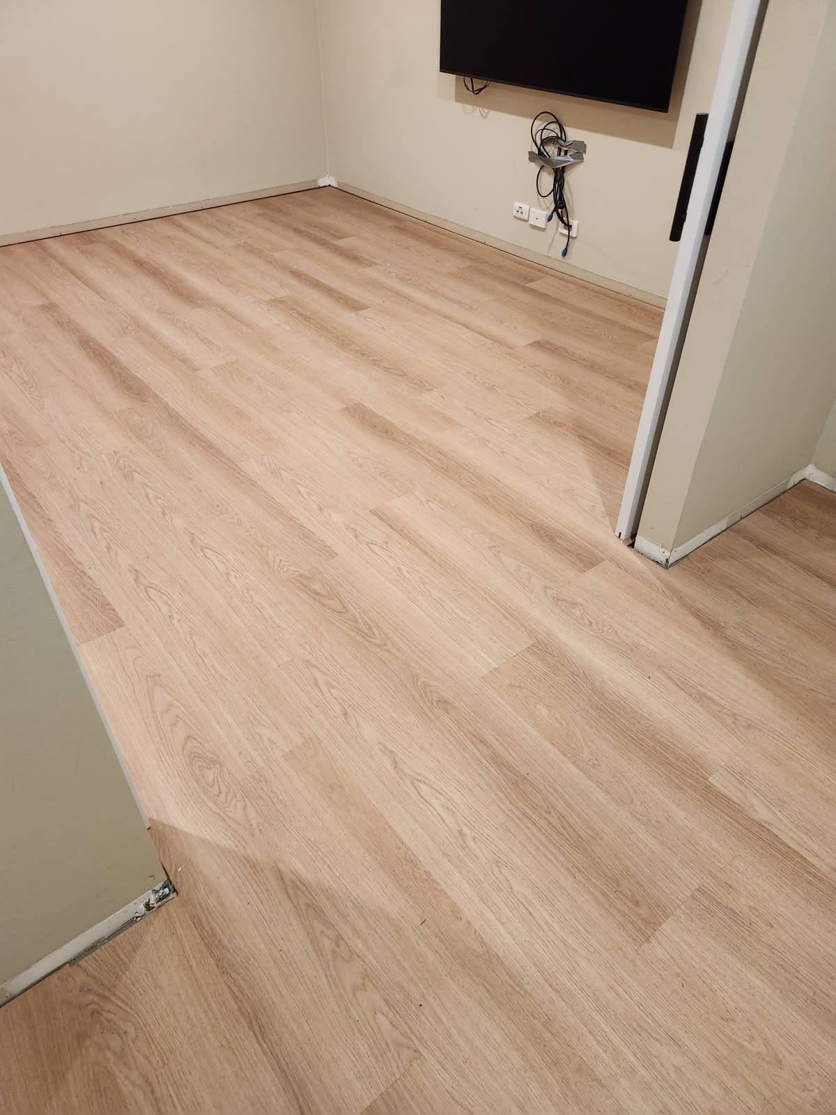 Light Wood-Look Flooring in A Room with A Tv Mounted on The Wall and A Door Frame — Canberra Floor Coverings in Queanbeyan West, NSW