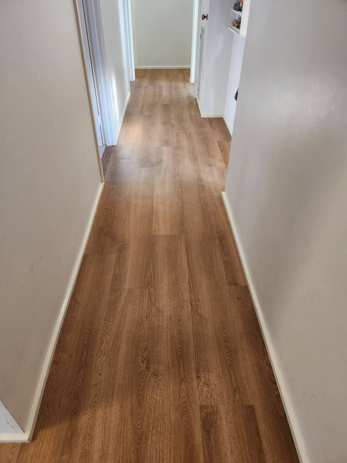 A Narrow Hallway with Brown Wood-Look Flooring, Beige Walls, and White Trim — Canberra Floor Coverings in Queanbeyan West, NSW