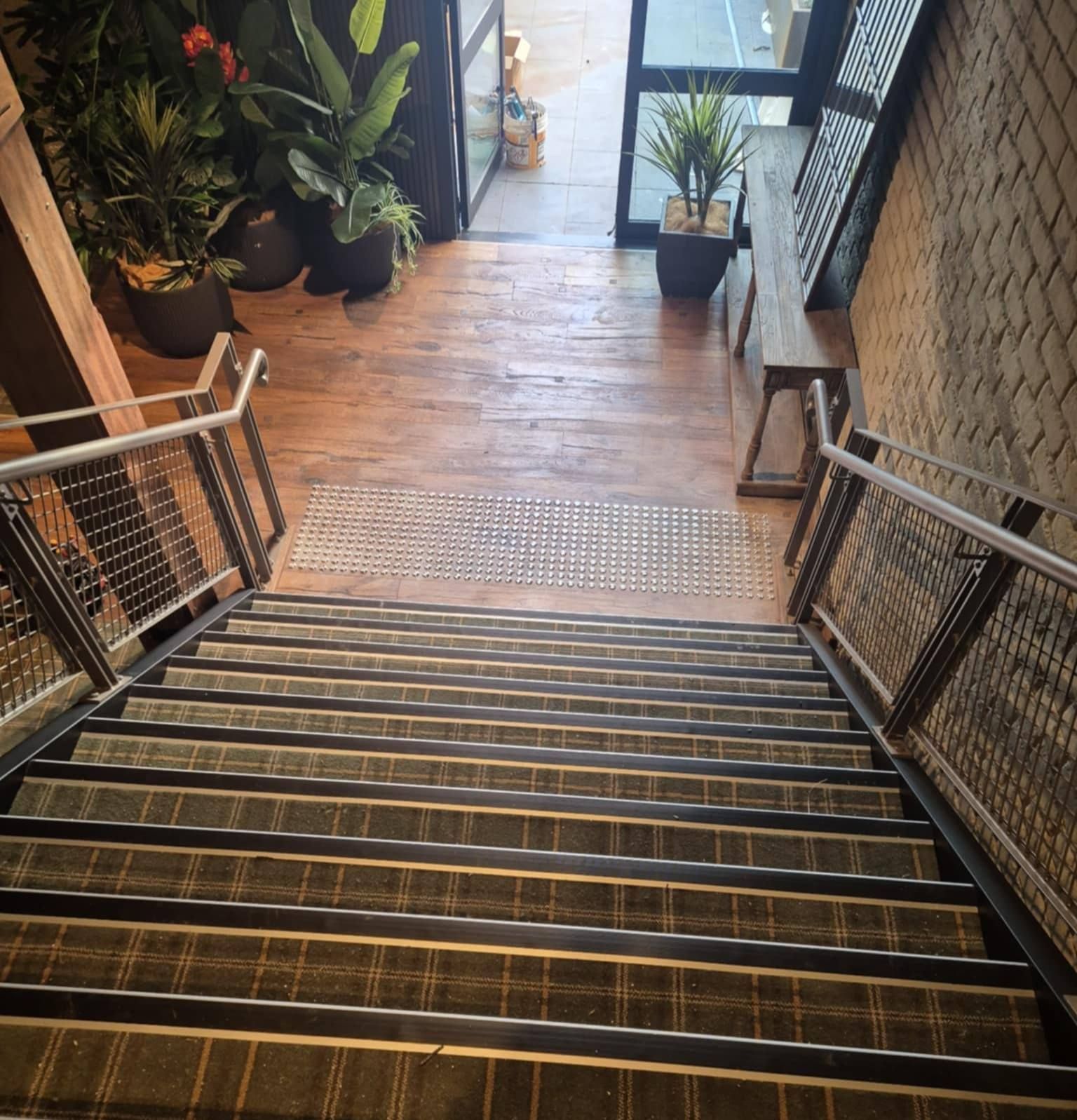 Staircase Descends Into a Building, with Wooden Steps and Metal Handrails. Plants and A Window Are at The Top — Canberra Floor Coverings in Queanbeyan West, NSW