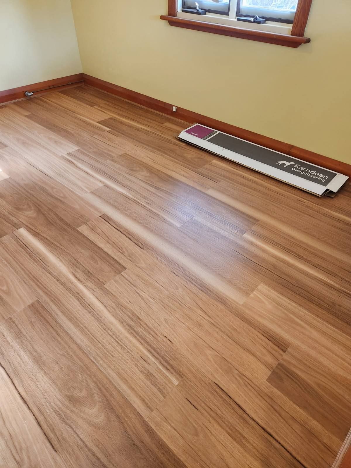 Wooden Floor in A Room with Yellow Walls, a Window, and A Flooring Installation Tool — Canberra Floor Coverings in Queanbeyan West, NSW