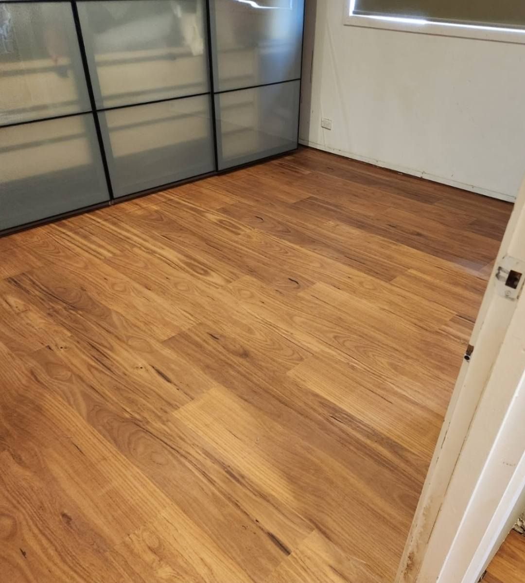 Wooden Floor in A Room with A Closed Cabinet on The Left and A White Door on The Right — Canberra Floor Coverings in Queanbeyan West, NSW