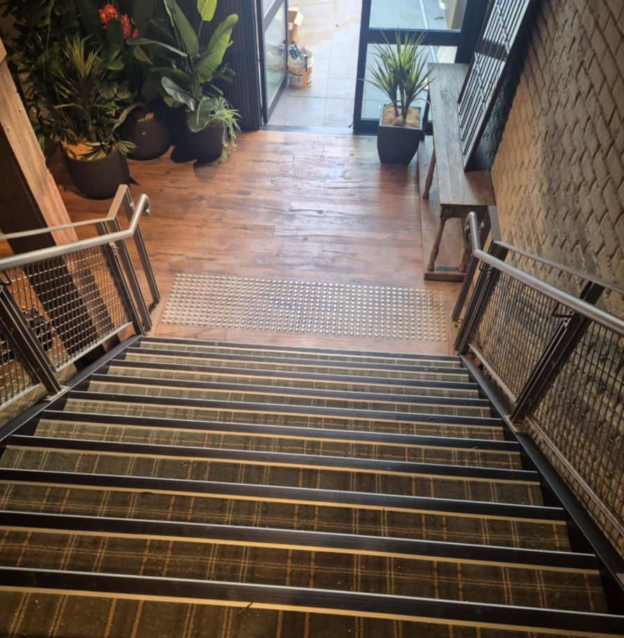 Staircase Leading Downwards. Wooden Steps with Metal Handrails, Plants, and A Brick Wall — Canberra Floor Coverings in Queanbeyan West, NSW