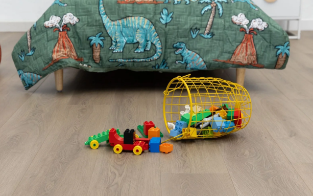 Dinosaur-themed quilt with a tipped yellow basket of building blocks on the floor.