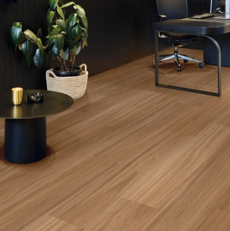 Wooden floor in a room with a plant in a basket, a black table with decor, and a desk.