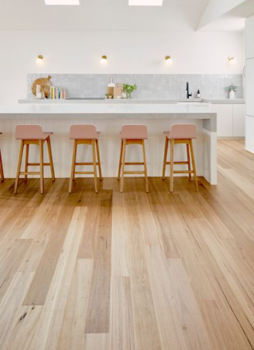 Kitchen with light wood floors, white island with pink stools, and marble backsplash.