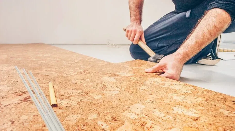 Person Installing Cork Flooring with A Hammer on A White Floor — Canberra Floor Coverings in Queanbeyan West, NSW