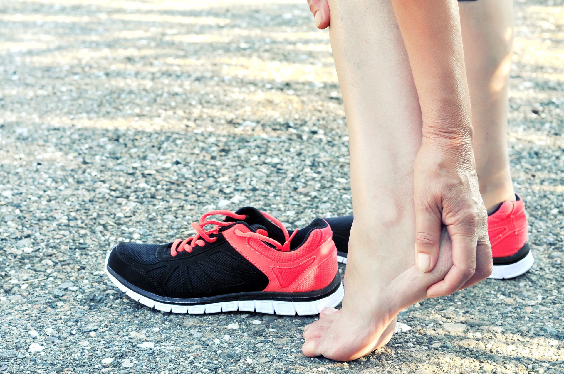 Person touching their heel next to a running shoe on a textured ground, indicating pain or discomfort.