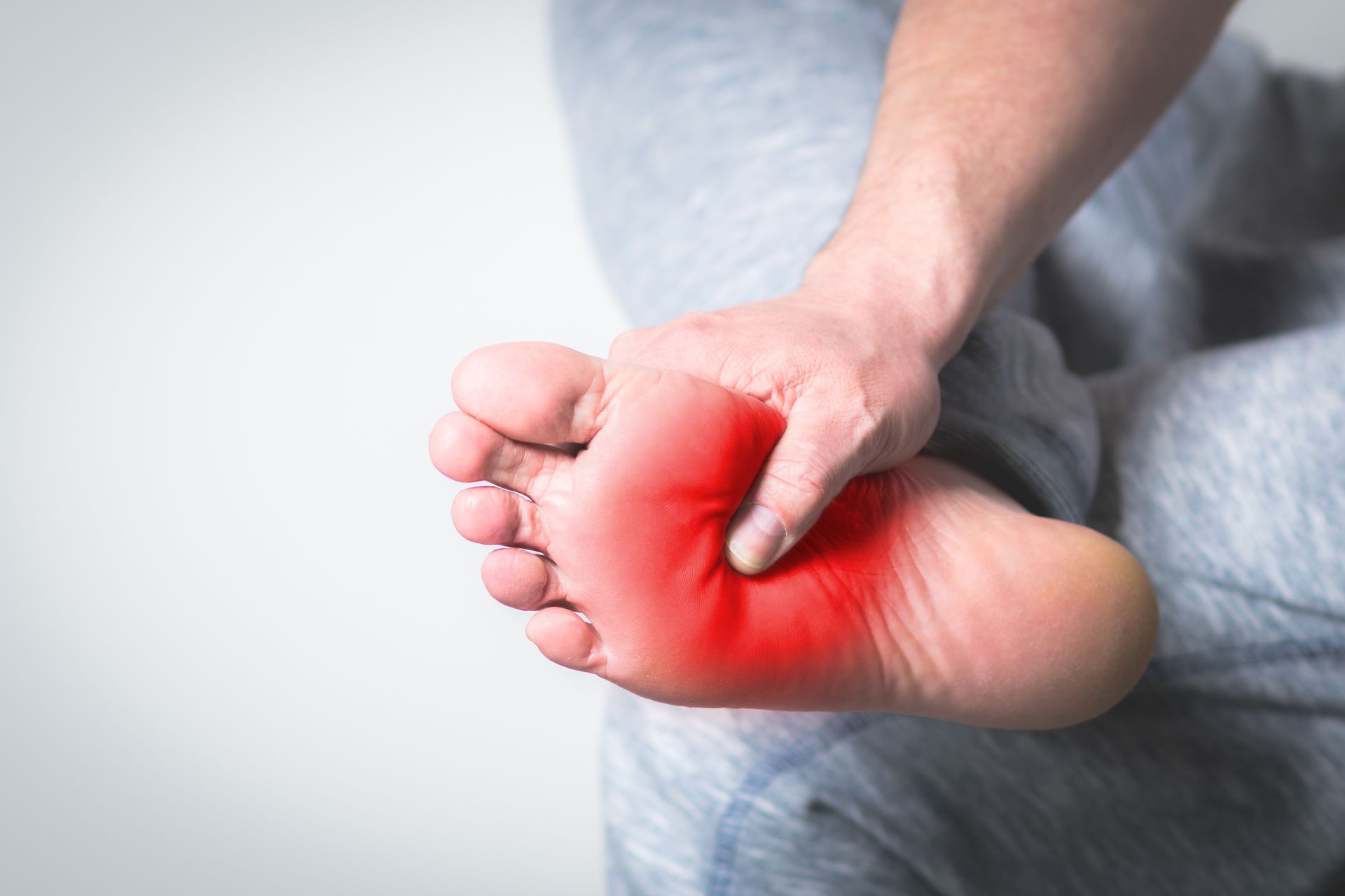 Person holding their foot, highlighting the red, inflamed arch, likely indicating pain.