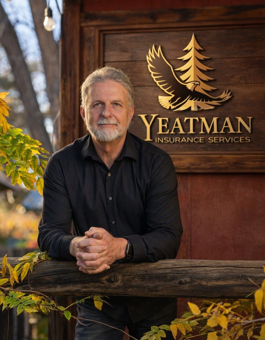 Man in black shirt leaning on wooden rail, in front of a sign for Yeatman Insurance Services.