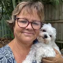 A Woman Wearing Glasses Is Holding A Small White Dog — Yeppoon Boarding Kennels & Cattery In Farnborough, QLD