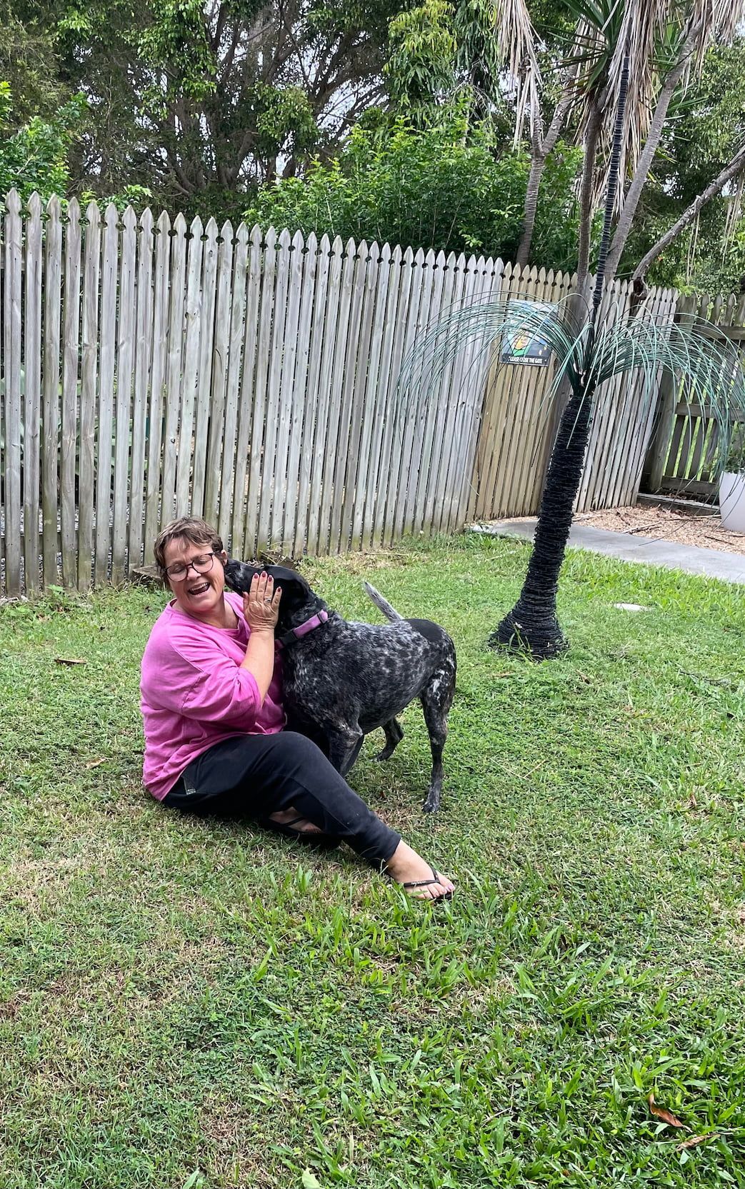 A Woman Is Sitting On The Grass With A Dog — Yeppoon Boarding Kennels & Cattery In Farnborough, QLD