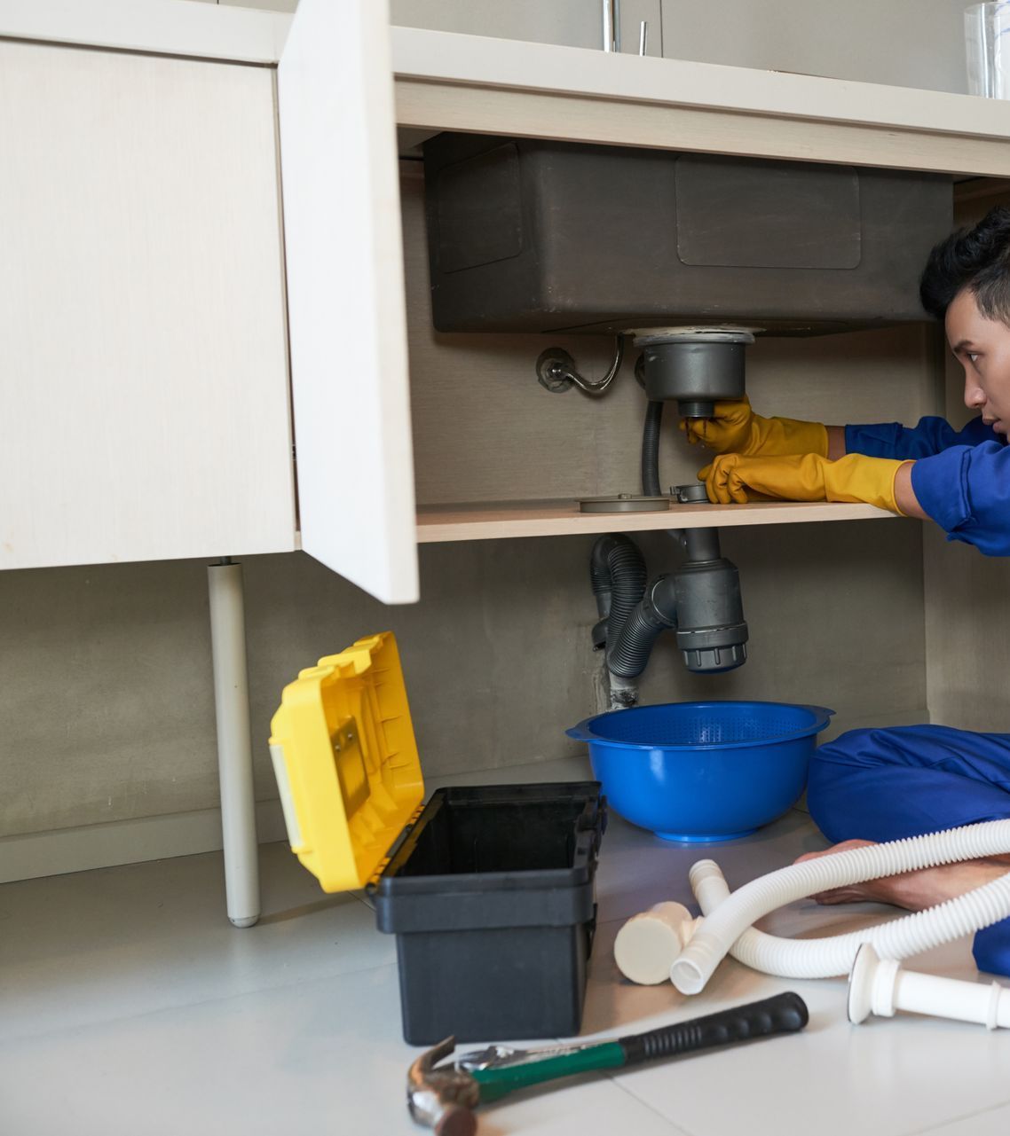 A plumber is fixing a sink in a kitchen.