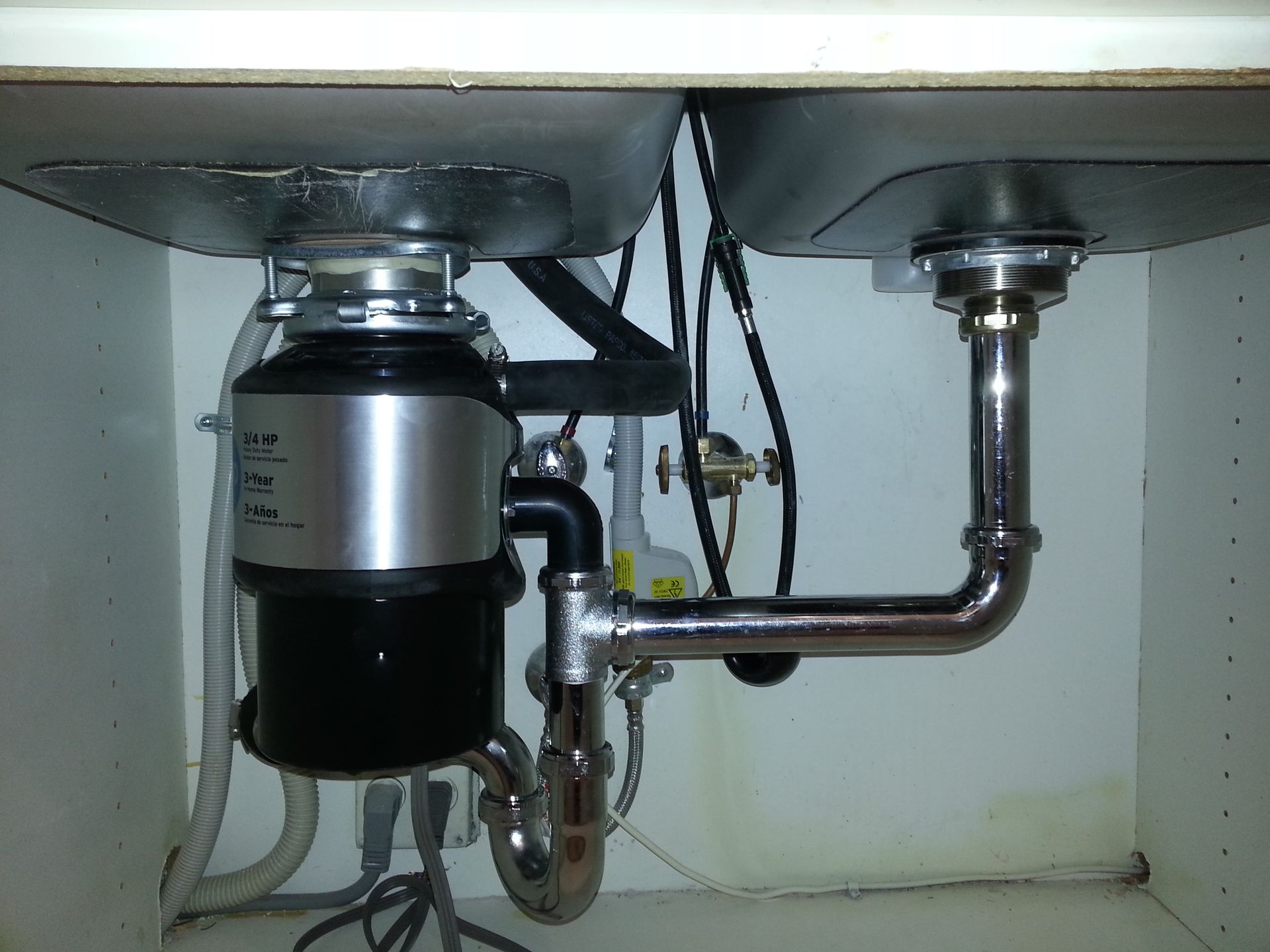 Under-sink plumbing with a garbage disposal and drain pipes in a white cabinet.
