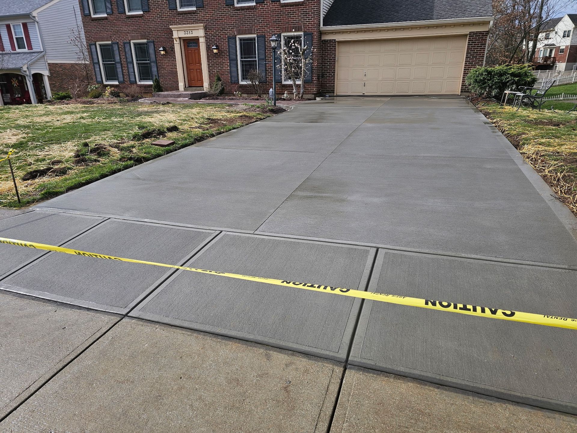 A concrete driveway in front of a house with a yellow caution tape.
