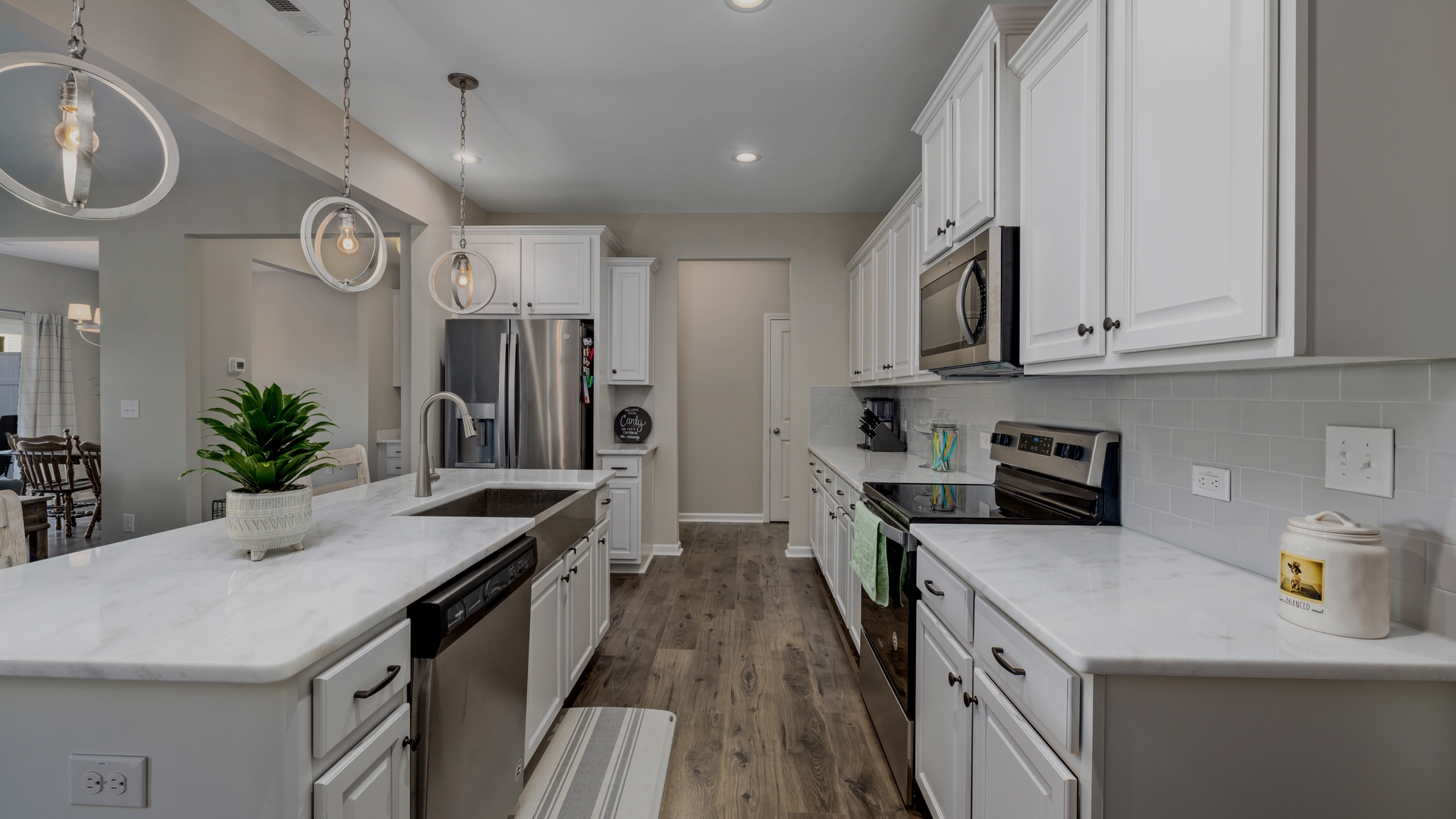 Modern white kitchen with stainless steel appliances, white countertops, and wood-look flooring.