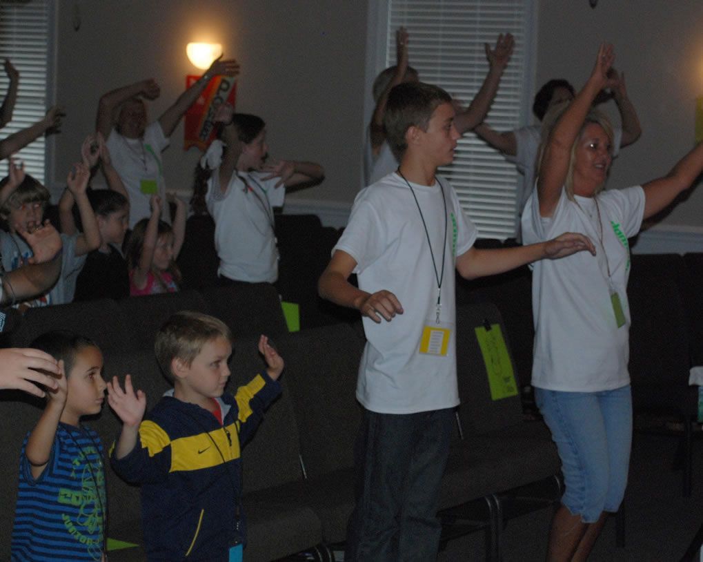 A group of children are standing in a room with their arms in the air