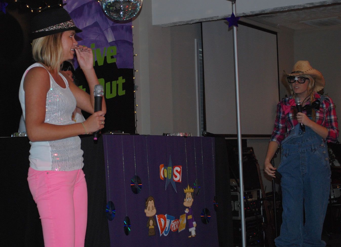 A girl singing into a microphone next to a man in overalls