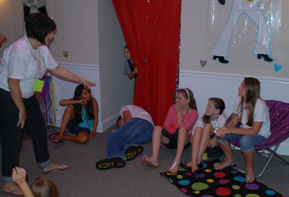 A woman is pointing at a group of children sitting on the floor