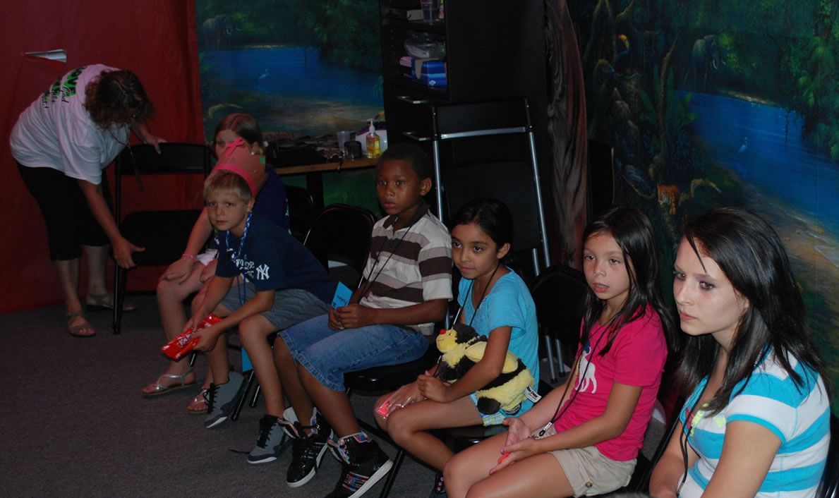 A group of children are sitting in chairs playing a video game.