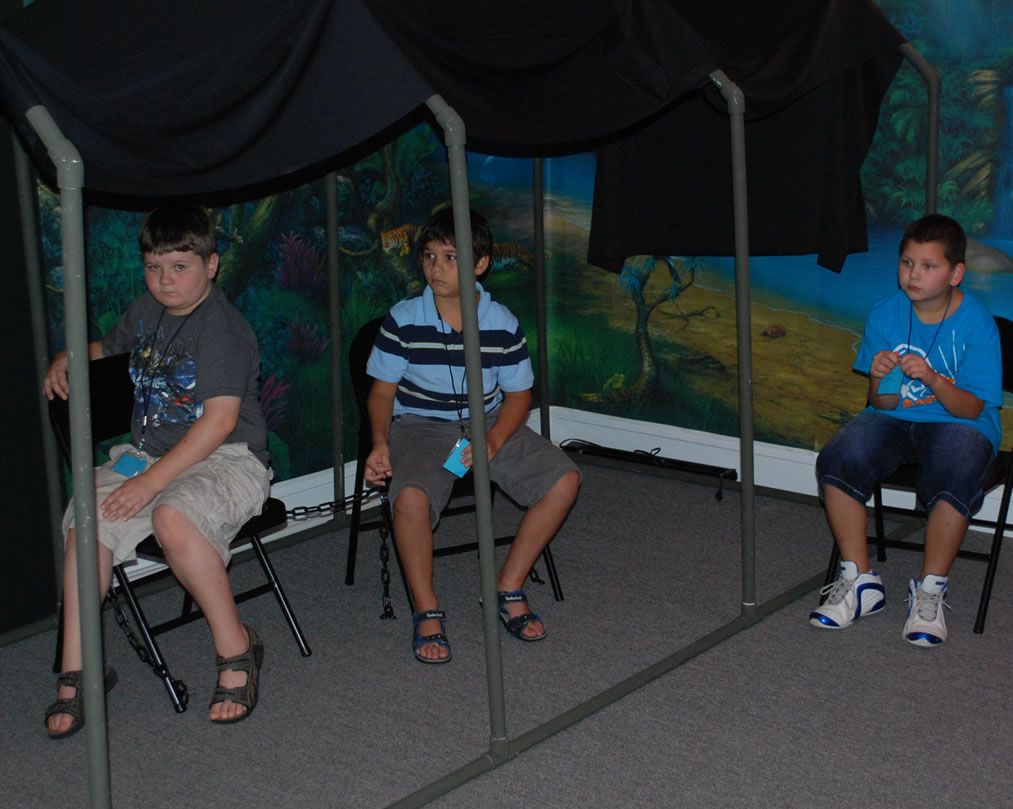 Three young boys are sitting under a canopy in front of a painting