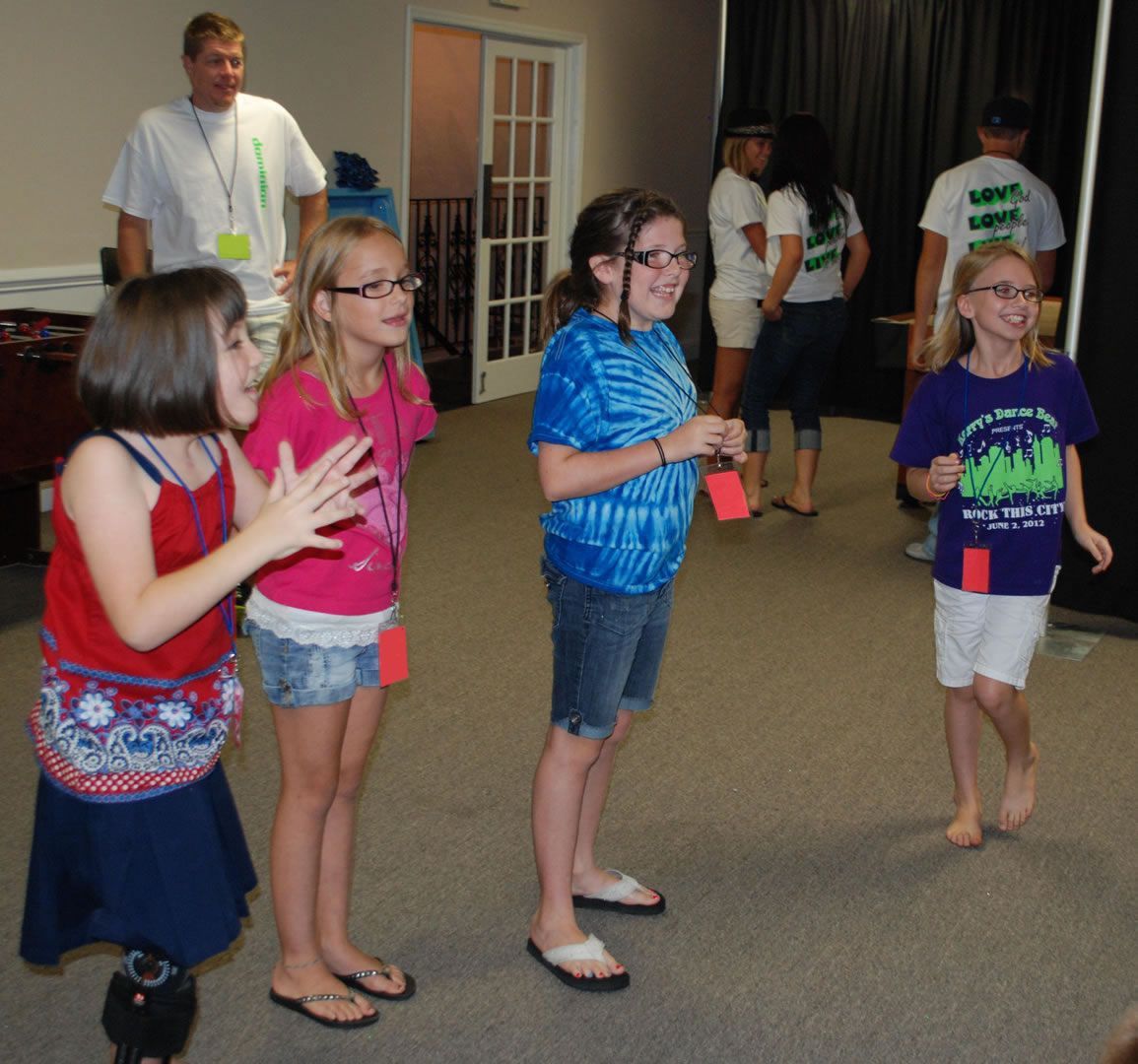 A group of young girls are standing in a room and one of them is wearing a shirt that says 