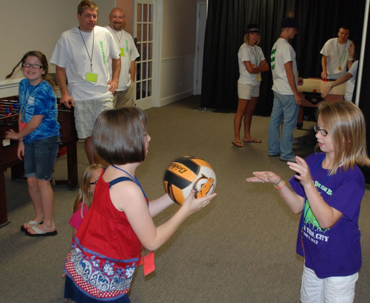 A girl in a purple shirt is throwing a volleyball to another girl