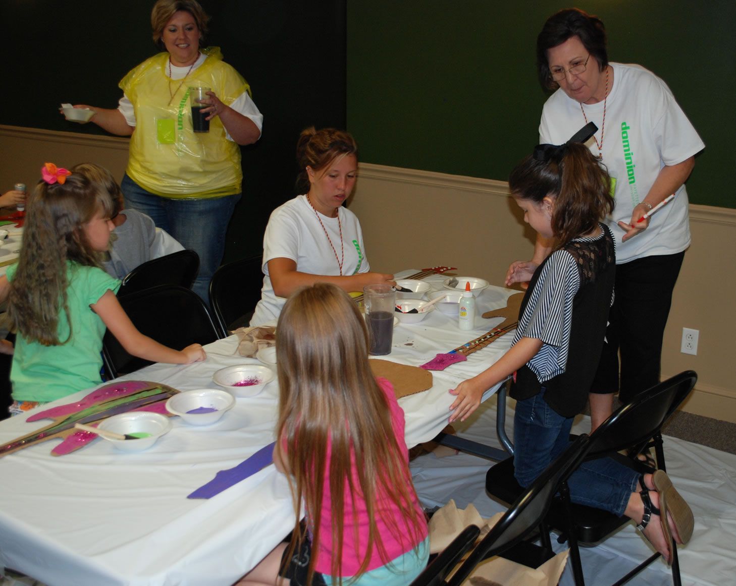 A group of children are sitting at a table with a woman standing behind them