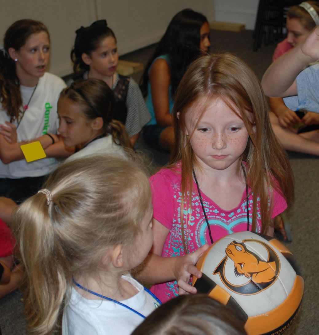 A girl in a pink shirt is holding a soccer ball