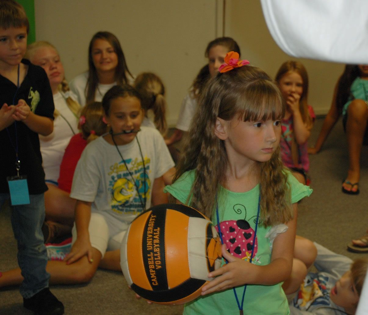 A girl in a green shirt is holding a volleyball with the word volleyball on it
