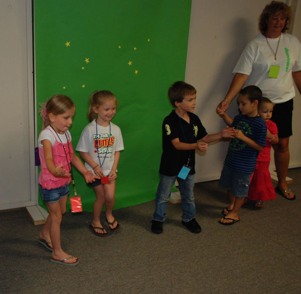 A group of children are holding hands in front of a green backdrop