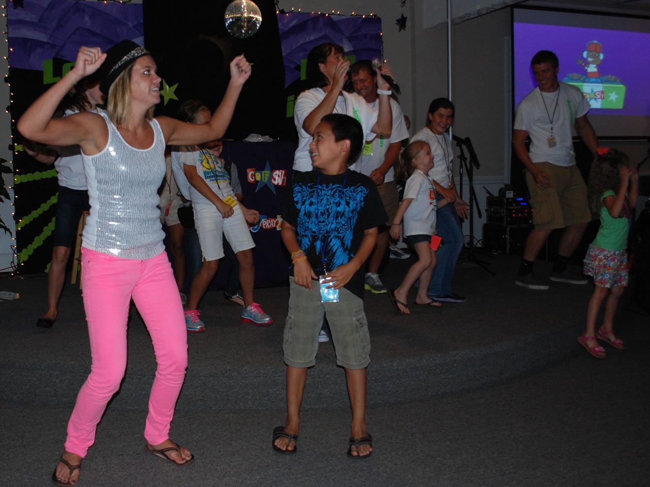 A woman in a silver tank top is dancing with a boy in a black shirt